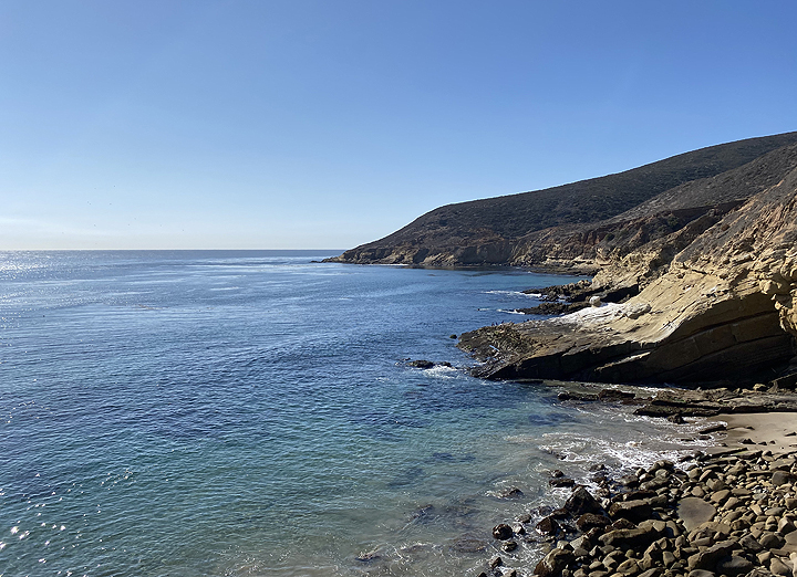 view of rocky beach and hilly coastline on a sunny day